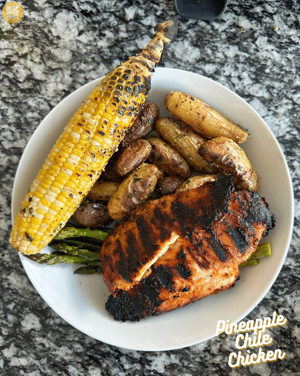 a plate of Pineapple Chile Chicken, grilled corn on the cob, asparagus, and fingerling potatoes 