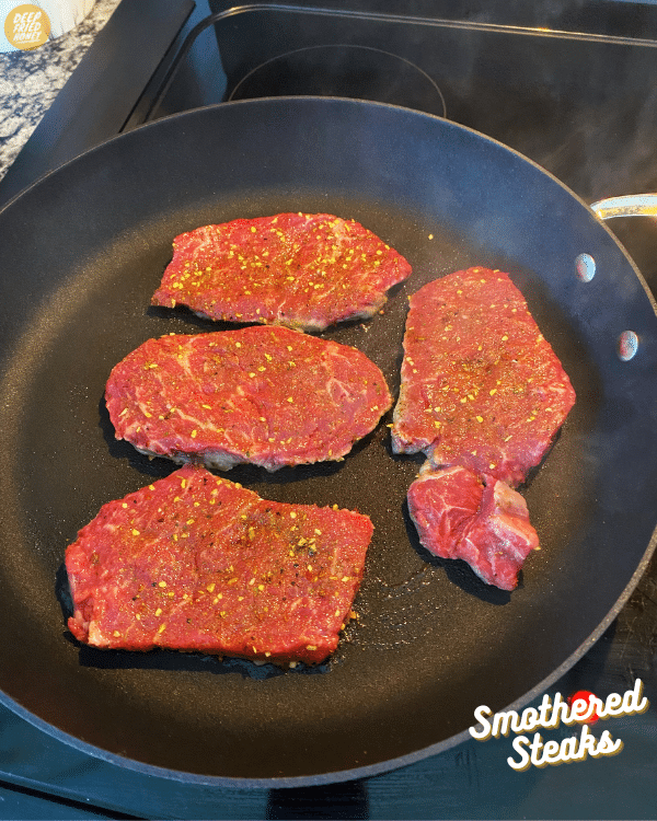 seasoned steaks being seared in a pan 